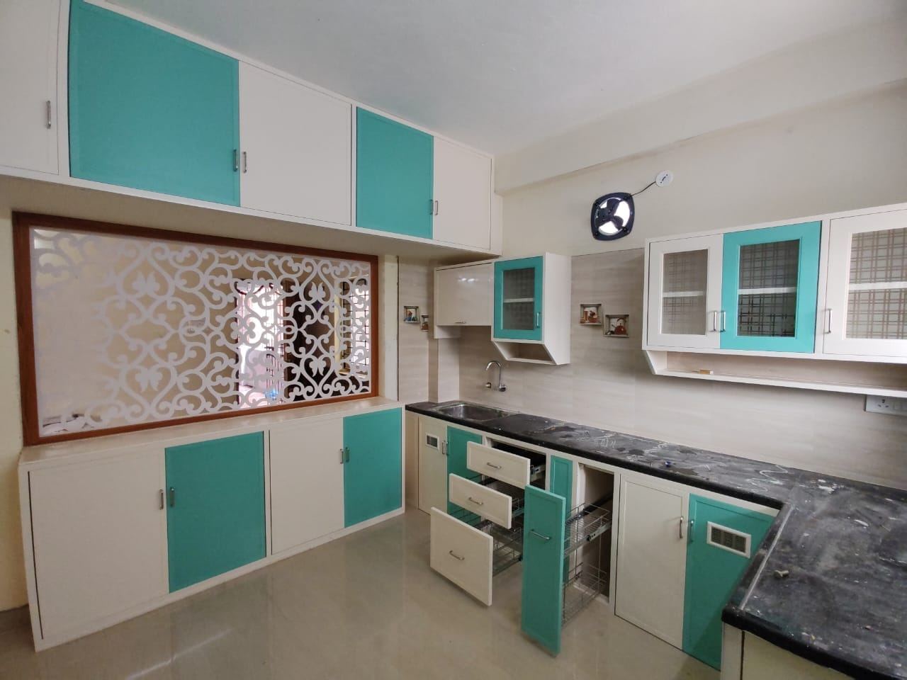 Teal and white PVC/uPVC modular kitchen with a decorative jali partition and pull-out wire baskets